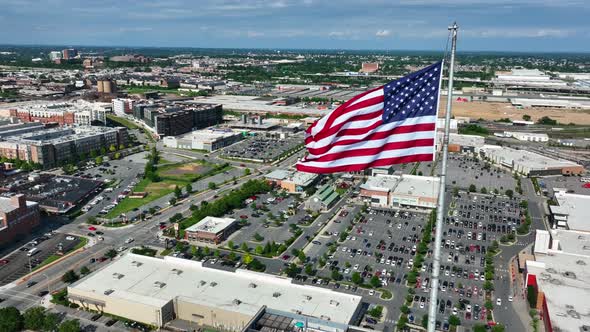 American flag proudly flies over urban city in USA. Retail shopping mall, office building, homes and