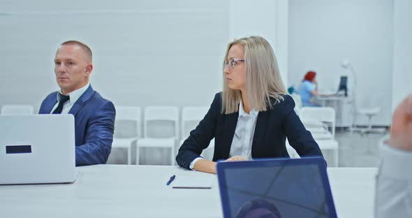 Young Beautiful Business Woman with Glasses Sits at a Table in a Conference Room She Speaks and