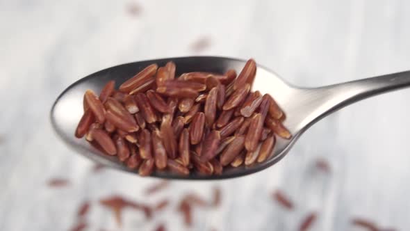 Brown rice falls out of a metal spoon