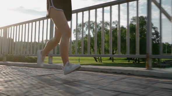 SLOW MOTION CLOSE UP Female Running in Green Park in Small Suburban Town with Tall Buildings in the