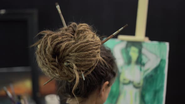 Rear View of Female Painter with Dreadlocks Fixed By Brushes Painting on Canvas at Easel