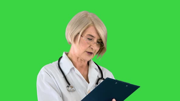 Serious Mature Doctor Woman Writing in Clipboard on a Green Screen Chroma Key