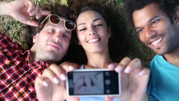 Three young adults taking a selfie lying on the grass