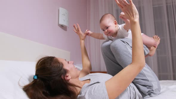 Happy Healthy Young Adult Mum Lifting Cute Infant Child Daughter Up Playing Airplane on Bed