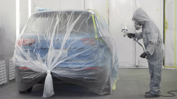 Auto painter painting car in a paint chamber