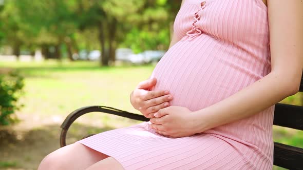 Close Up of Pregnant Woman Hands Stroking Belly on a Park Bench in the Summer