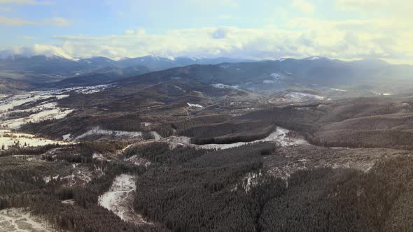 Aerial view of barren mountain landscape with falling snow over winter dark forest.