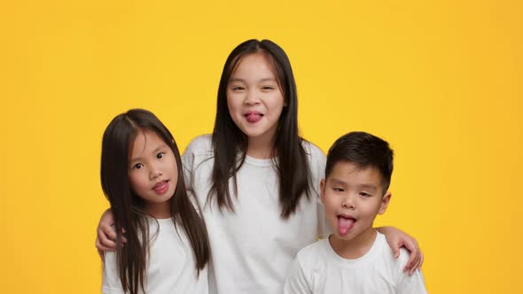 Cheerful Japanese Siblings Having Fun Grimacing Showing Tongues Yellow Background