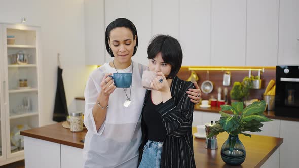 Happy Lesbian Couple is Drinking Coffee in the Kitchen Embracing