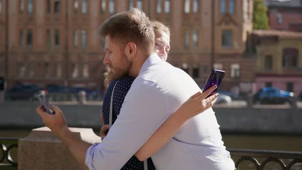 Side View of Young Couple Hugging and Using Smartphone Outdoors