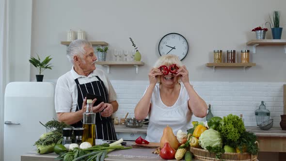 Senior Couple Cooking Salad with Vegetables. Woman Dancing Holding Fresh Slices of Pepper on Eyes