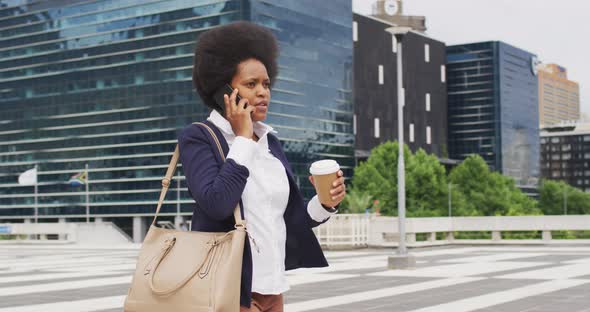 African american businesswoman holding takeaway coffee and talking on smartphone