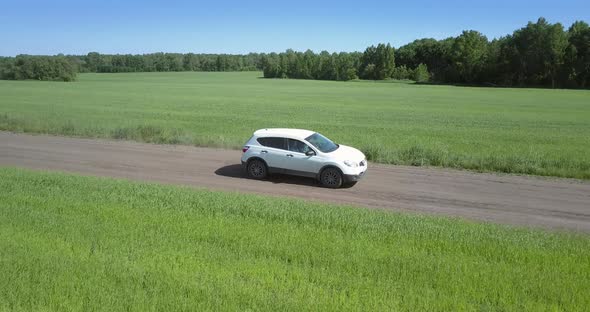 Fast Car Speeds Along Path Between Boundless Green Fields