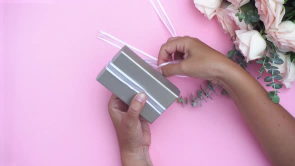 Someone Hands Wrapping Gift or Present Box and Flowers on Pink Table