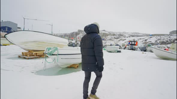 Man In Winter Coat Walking Towards Moored Boat In Snow Ilulissat