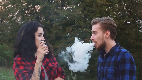 Young Beautiful Couple Vaping E-cigarette in the Park