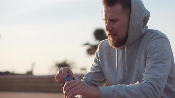 Exhausted Sportsman Is Resting Outdoors and Drinking Water