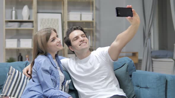 Young Couple Taking Selfie with Smartphone While Sitting on Couch