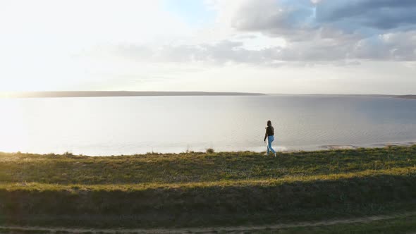 Tracking Aerial Shot of Young Woman Enjoying Sunset in Field Near the Cliff During Beatiful Sunset