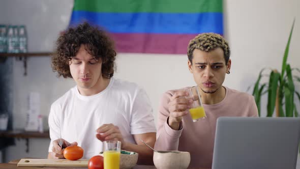 Beautiful Couple Gay on the Kitchen Together Preparing Breakfast Watching News on Laptop