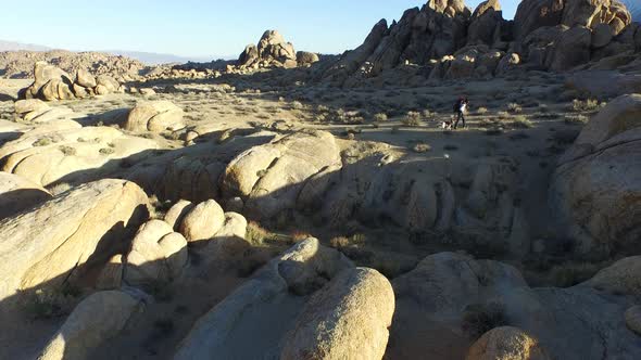 Aerial shot of a young man backpacking with his dog in a mountainous desert.