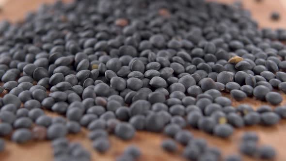 Black raw lentils are scattered on the board in slow motion. Uncooked legumes. Macro