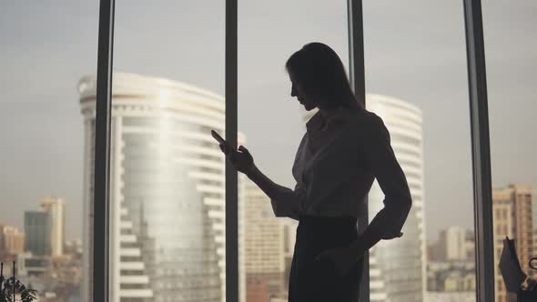 Silhouette of a Young Woman Against the Background of a Large Window and Skyscraper
