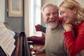 Smiling Senior Couple At Home Enjoying Learning To Play Piano - PhotoDune Item for Sale
