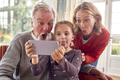 Grandparents With Granddaughter Pulling Faces Posing For Selfie On Mobile Phone At Home Together - PhotoDune Item for Sale