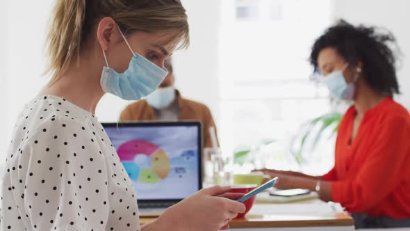 Woman wearing face mask using smartphone at office