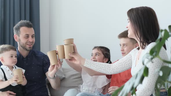 Happy Mom Dad and Three Children Sitting on the Couch Holding Glasses and Drinking Juice