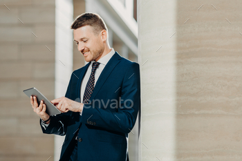Businessman reads news in internet on web page, uses touch pad, dressed in elegant suit.