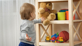 Cute baby boy taking teddy bear toy from bookshelf in playroom. Child education - PhotoDune Item for Sale
