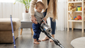 Young mother doing housework teaching and giving vacuum cleaner to her baby son. - PhotoDune Item for Sale