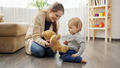 Happy smiling mother playing with her baby son with teddy bear on floor in living room. - PhotoDune Item for Sale
