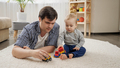 Young father lying with his baby son on carpet and playing toy cars. - PhotoDune Item for Sale