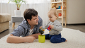 Young father lying on carpet with his baby son and playing with toys - PhotoDune Item for Sale