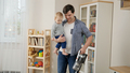 Young father holding his baby son while doing house cleanup and using vacuum cleaner. - PhotoDune Item for Sale