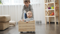 Older boy riding his baby brother in wooden toy cart in living room. - PhotoDune Item for Sale