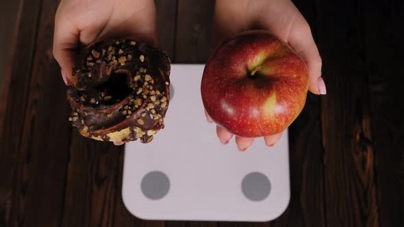 Closeup of a Woman Holding an Apple and a Doughnut While Standing on a Scale