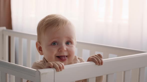 Closeup Shot Of Adorable Infant Baby Standing In His Crib And Grimacing