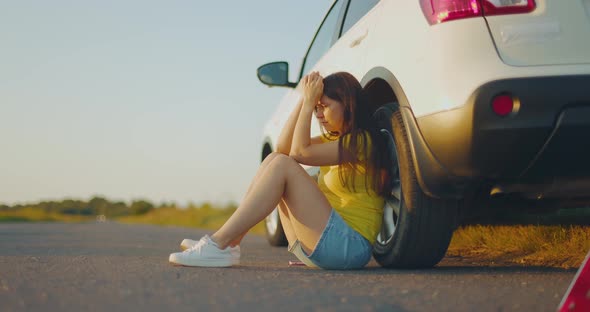 Upset Girl Sitting Next to Broken Car on Side of Road