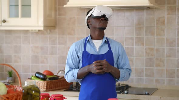 Medium Shot Young Man in Apron and VR Headset Standing in Kitchen Indoors with Ripe Vegetables