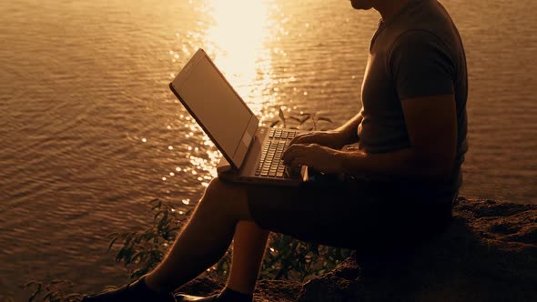 Young business man working on laptop at sunset. Freelance job online, focus on the screen