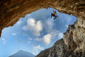 Male rock climber hanging with one hand on on a cliff against sky - PhotoDune Item for Sale