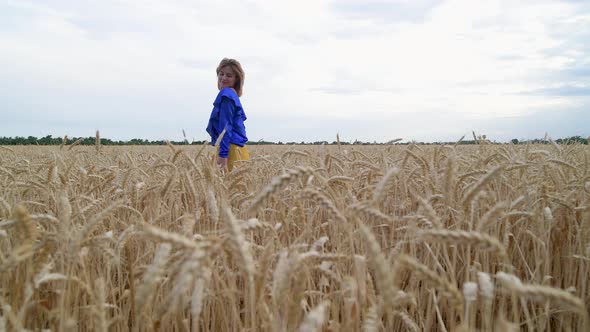 Beautiful Ukrainian Woman Wearing Dress in Ukrainian National Flag Colours Blue and Yellow at Wheat