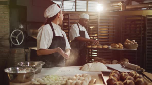 Animation of happy asian female baker cleaning hands from flour and talking with male coworker