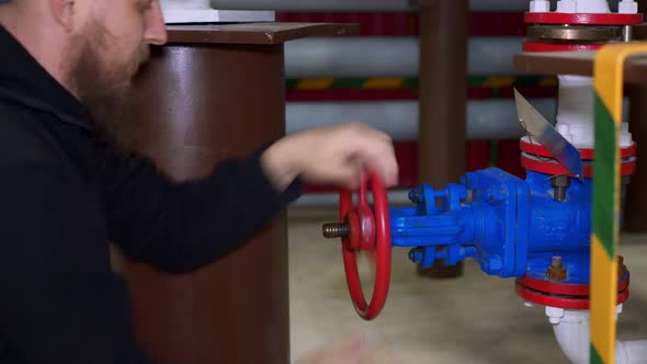 A Male Worker with a Beard Turns on the Valve of the Tap for Supplying Liquid From the Reservoir