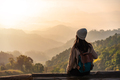 Happy young woman traveler relaxing and looking at the beautiful sunrise on the top of mountain - PhotoDune Item for Sale