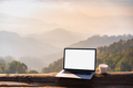 Empty screen laptop with cup of coffee and camera with mountain view at sunrise in the morning - PhotoDune Item for Sale